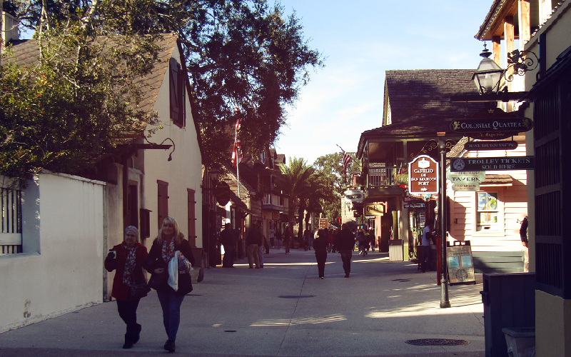 Image contains two people walking down a street with trees and building.