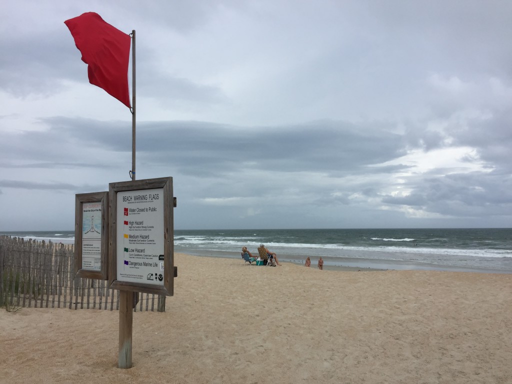 Image contains dark clouds rolling over a stormy sea and a beach warning flag.