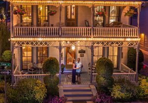 Front exterior view of 19th century building at dusk. Soft yellow lights run along the second floor balcony and first floor patio.