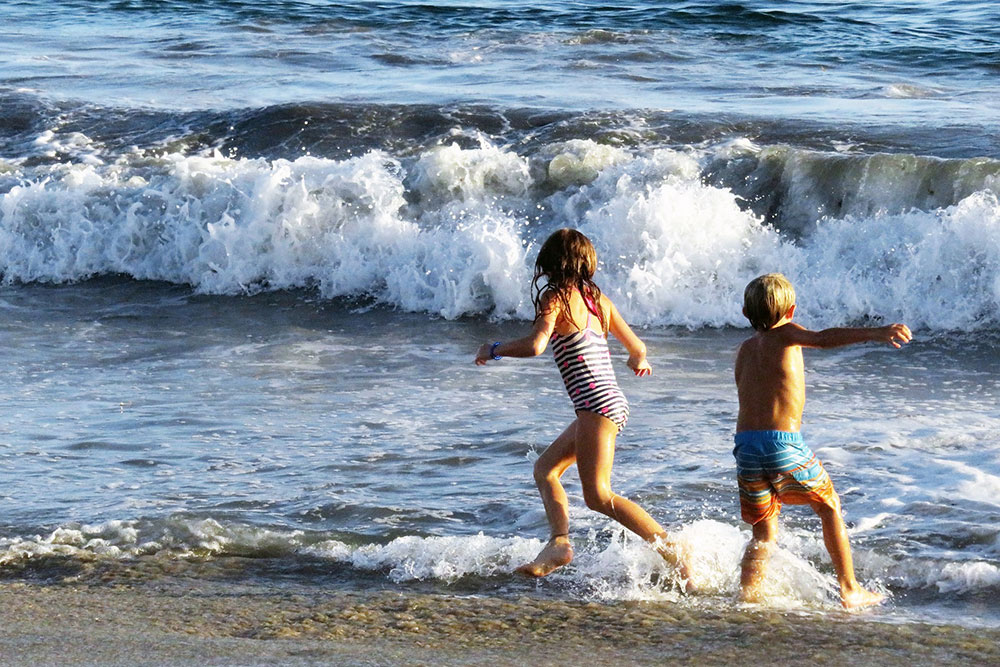 Two children (girl and boy) playing in the waves at the beach.