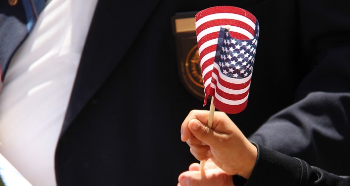 image of child's hand, in foreground, holding small American flag on stick; in background dark jacket with medals pinned to left side. Veteran's Day Memorial