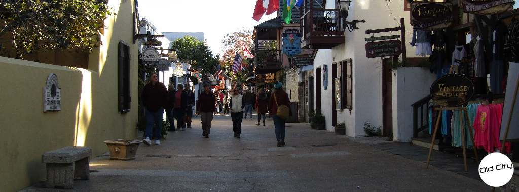 Image contains people walking on a street lined with shops and boutiques.