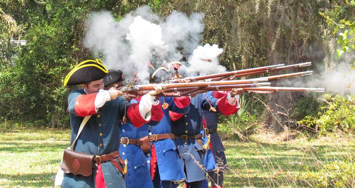 Reenactors dressed in 1700's garb, firing muskets during the Battle of Bloody Mose