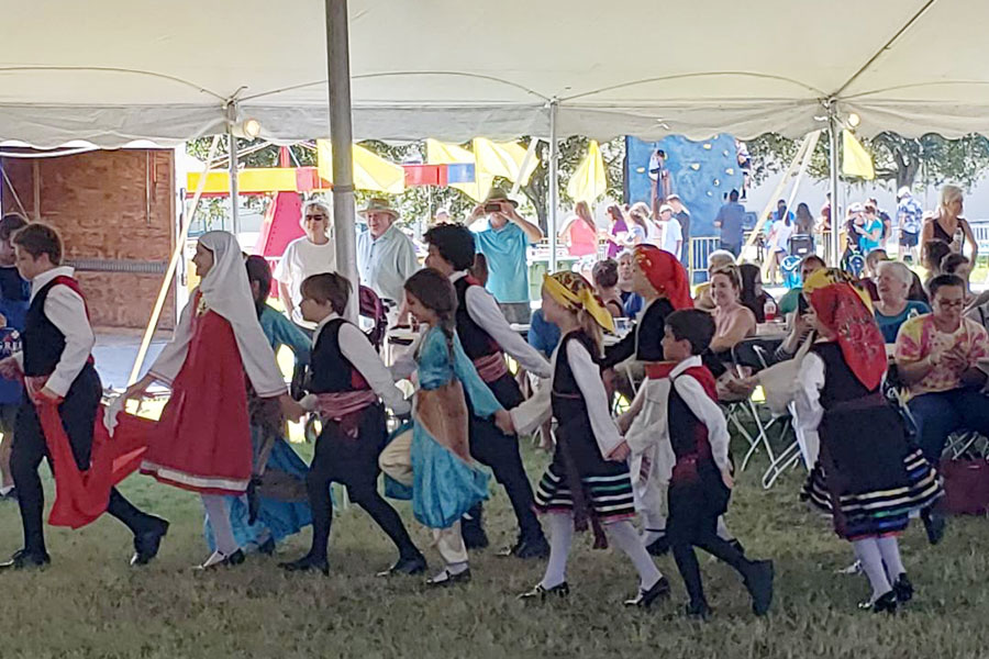 A group of children dancing in a line with people sitting in the background.