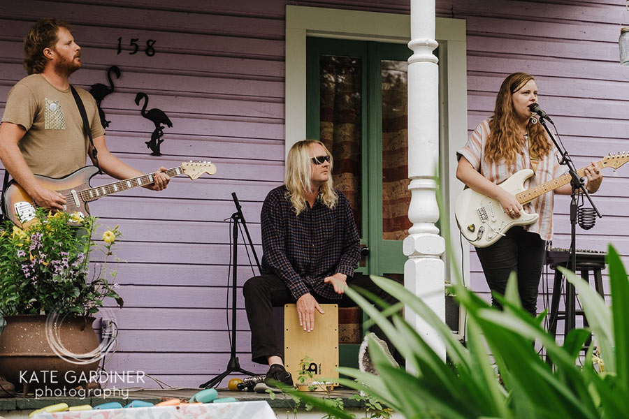 Two people playing the guitar and one person playing a drum on the front porch of a house.