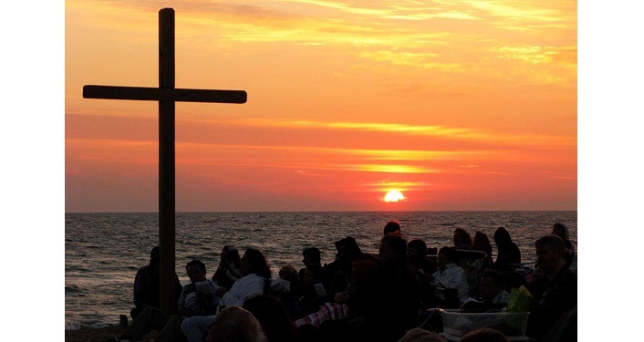large cross and people on the beach watching sunrise on Easter Sunday