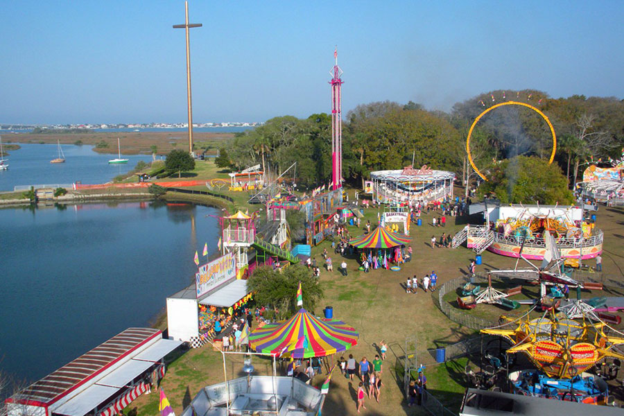 An aerial view of a large park that has theme park rides, people walk, and a giant cross.