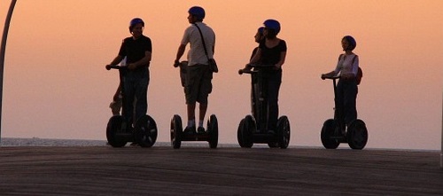 Image is of four people riding Segways on a boardwalk during sunset.
