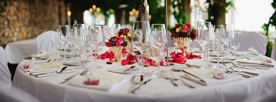 Image contains a table with silverware, plates, wine glasses, and flowers