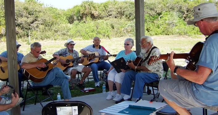 image of men and women sitting under covered pavilion; some playing guitars, some banjo, some mandolin at Gamble Jam Gamble Jam Session
