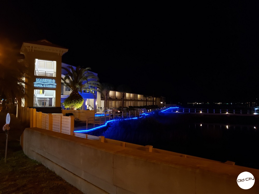 Image contains a marina next to a hotel that is decorated in lights.