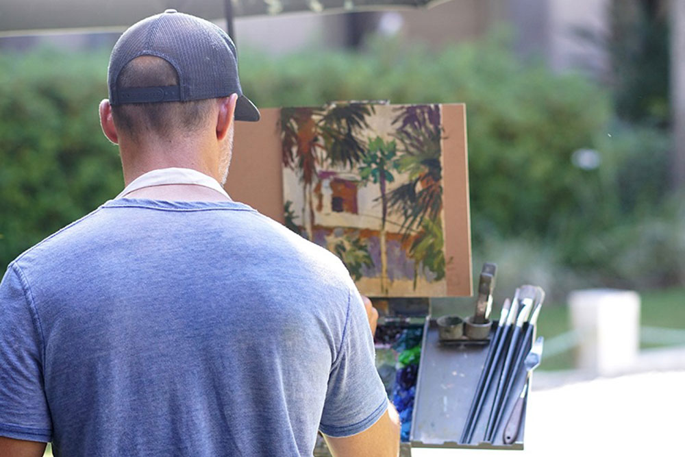 Over the shoulder shot of a man in a baseball cap painting St. Augustine scenery.