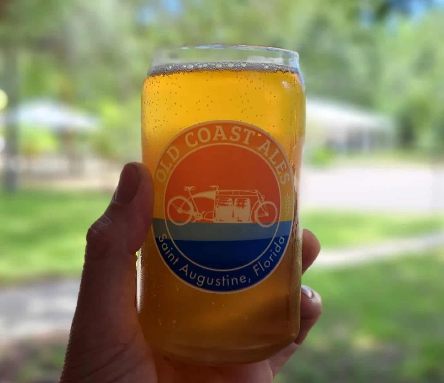 Closeup of someone holding a glass of beer with the Old Coast Ales logo on it.