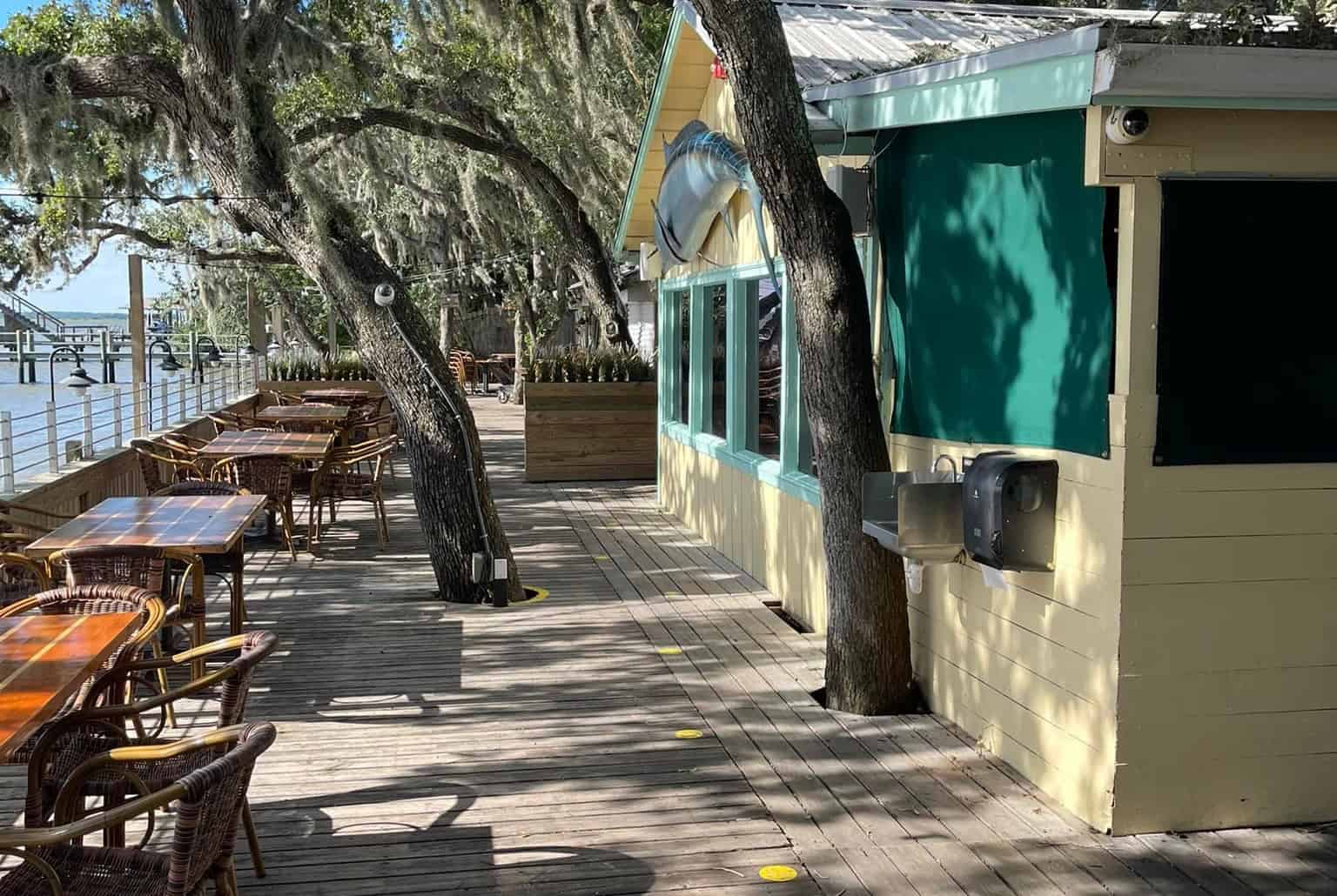 Patio seating outside Cap's On The Water Restaurant with trees and a waterfront view.