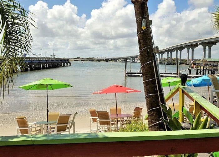 View of a sandy shore with colorful umbrellas and water from the patio seating area at the Beaches at Vilano restaurant in St. Augustine.