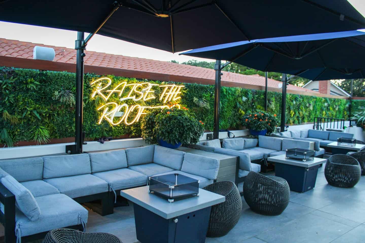 Couches and tables under awnings with bushes in the background on the patio at River & Fort in St. Augustine.