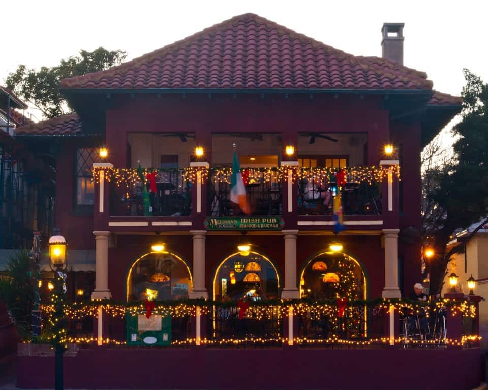 Exterior view of Meehan's Irish Pub decorated with festive lights, featuring an inviting upper balcony and a warm atmosphere in St. Augustine.