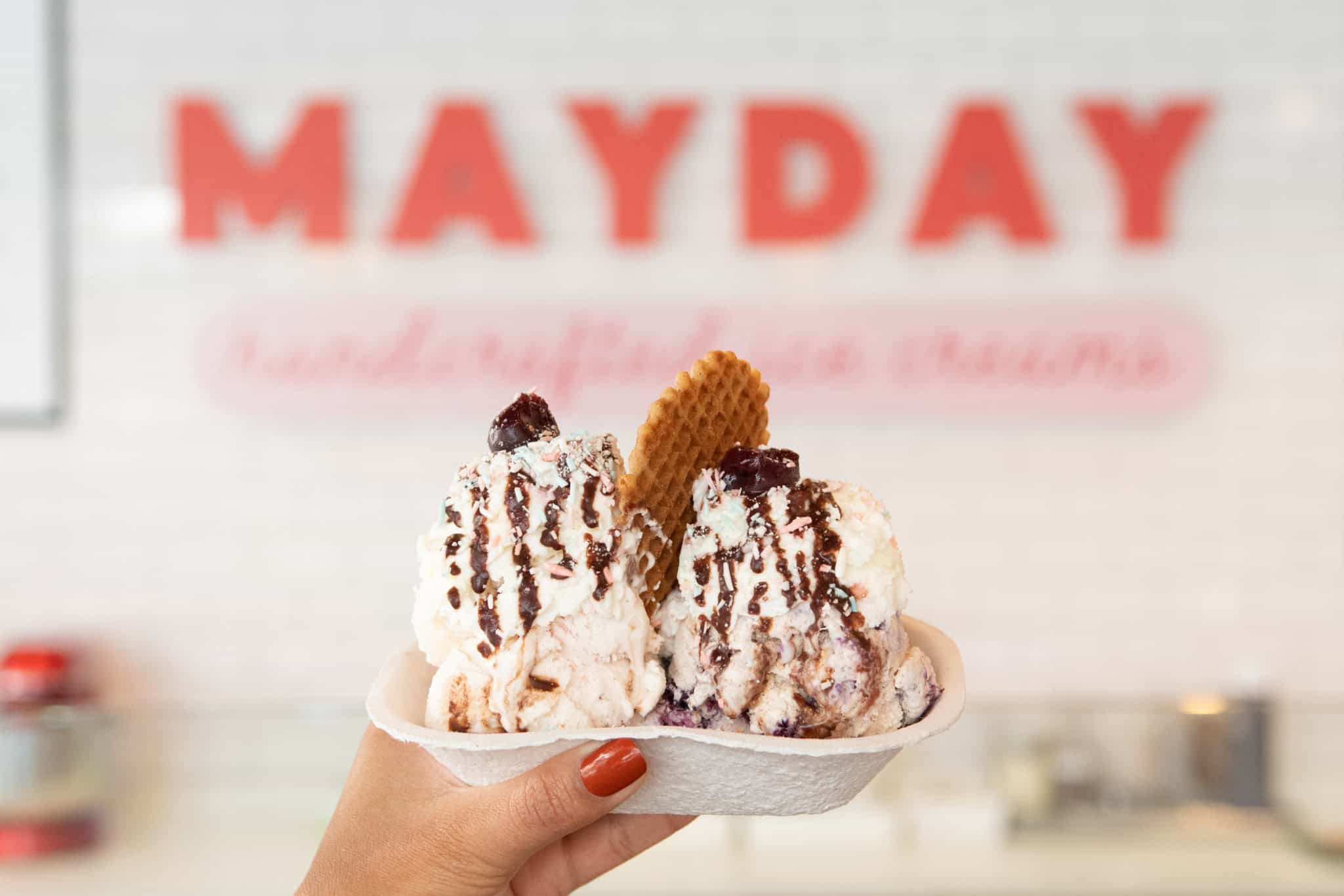 A sundae with whipped cream, chocolate fudge, and a waffle cone cookie in front of the Mayday sign.