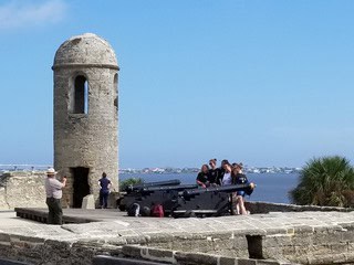 Tourists on the rampart of Castillo de San Marcos fort taking pictures next to canons and a watchtower