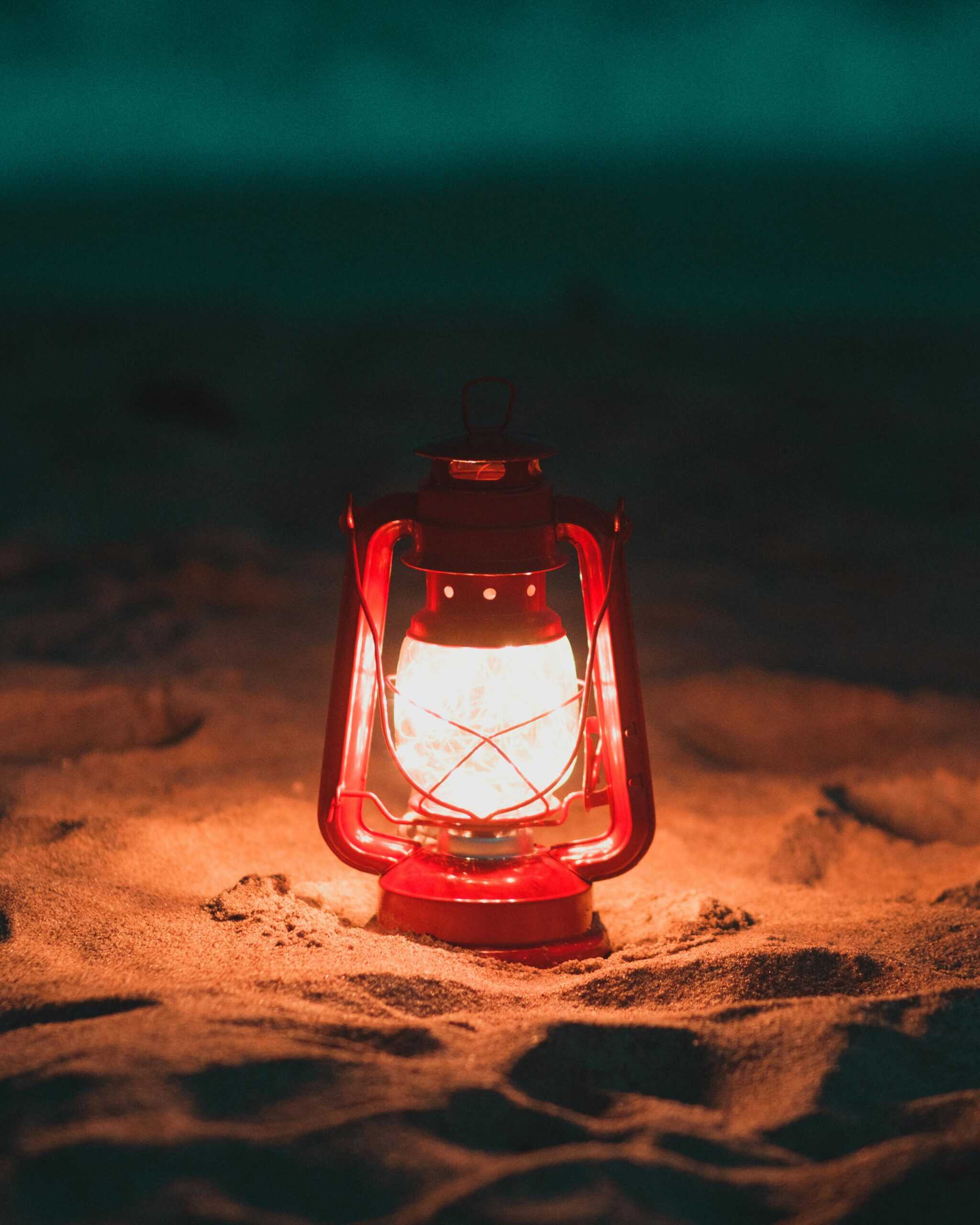 A glowing lantern sitting on a sandy beach