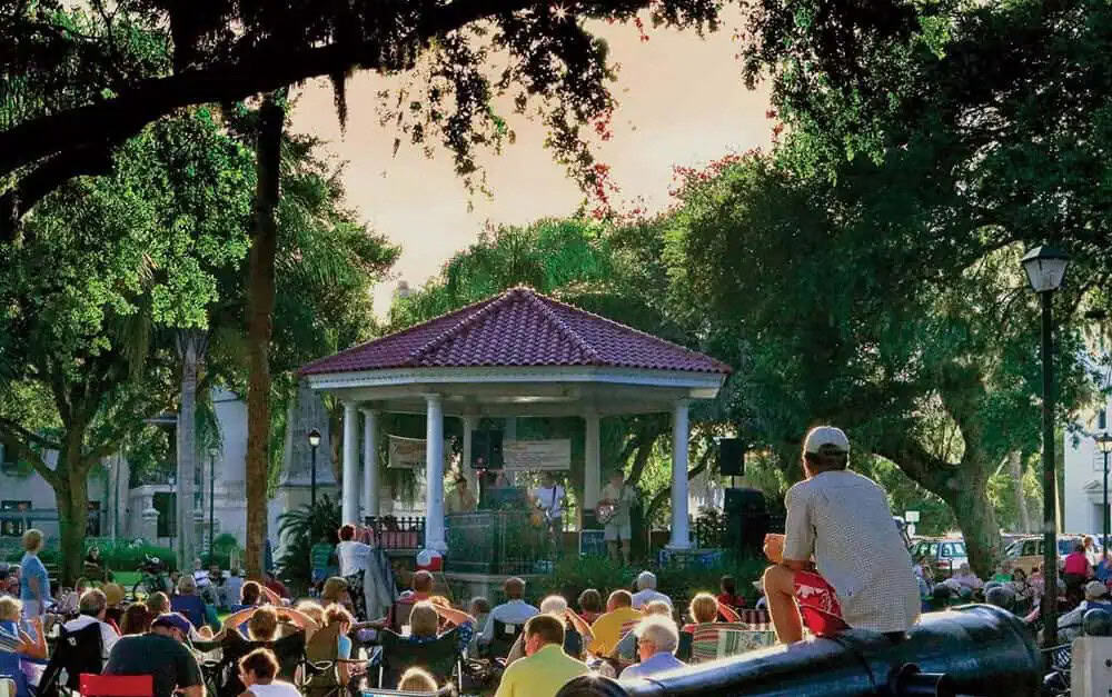 A crowd of people sitting around a gazebo in St. Augustine's plaza for a free concert.