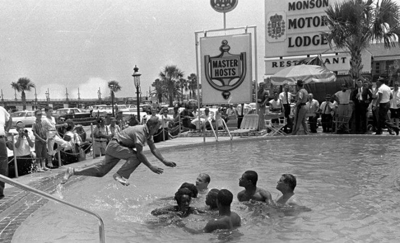 Black and white photo of white and black men swimming together in public pool in protest of segregation. 