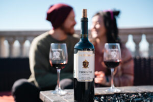 A bottle of San Sebastian wine and and two filled wine glasses set the forefront for a loving couple enjoying San Sebastian's balcony